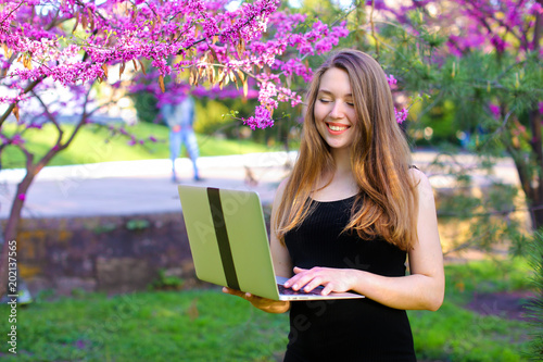 Pretty businesswoman working with laptop in blooming park background. Concept of modern , wirelees Internet and spring season. photo