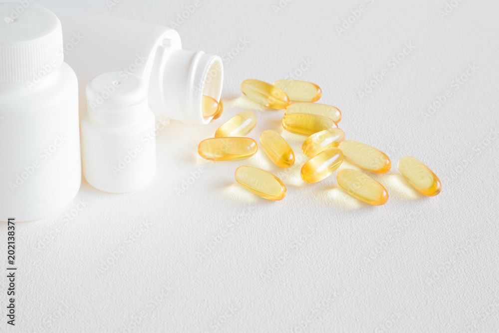 Fish oil capsules spilled out of white bottle on the table. Mock up for special offers as advertising or other ideas. Nutritional supplements and healthcare concept. Fish oil capsules spilled out of white bottle on the table. Mock up for special offers as advertising or other ideas. Nutritional supplements and healthcare concept.