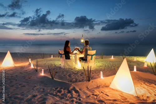 Paar sitzt beim privaten, romantischen Abendessen am tropischen Strand bei Sonnenuntergang photo