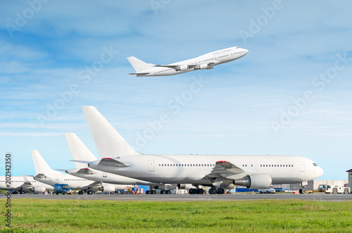 Passenger aircraft row, airplane parked on service before departure at the airport, other plane push back tow. One two-story airplane take off from the runway in the blue sky.
