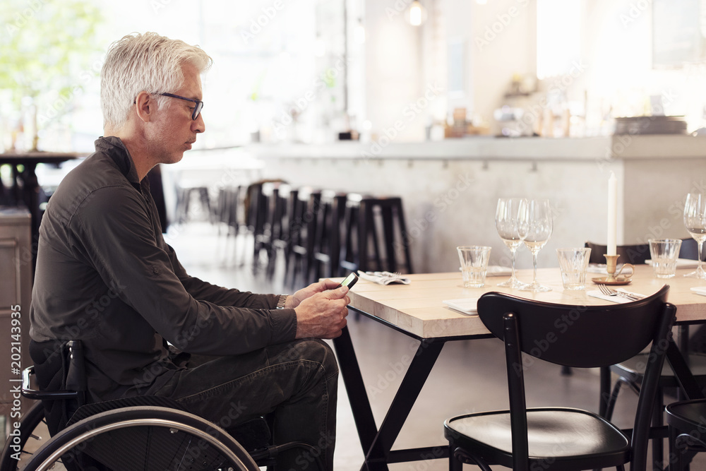 Man on wheel chair, using smartphone in restaurant Man on wheel chair, using smartphone in restaurant