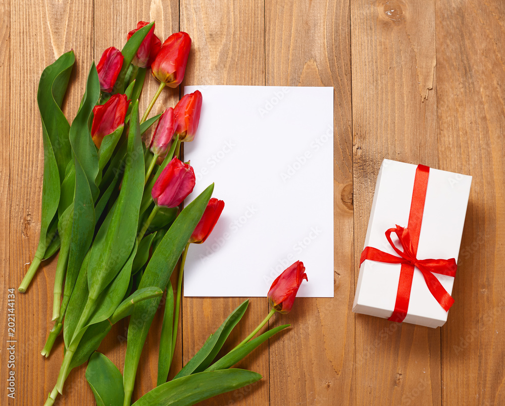 tulips are on wooden boards, blank paper sheet and gift, greeting concept