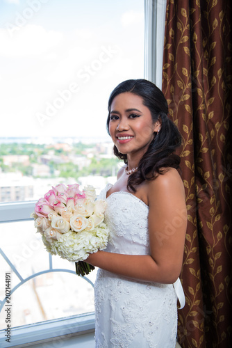 Portrait of Happy Smiling Bride with Her Bouquet Standing at a Window