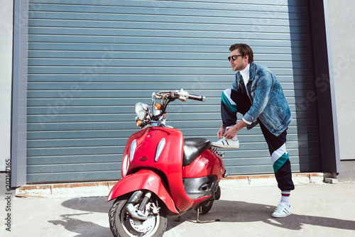 handsome young man in vintage clothing with red scooter lying up laces