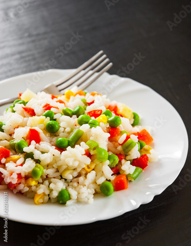 Rice with mixed vegetables on white plate. on dark wooden table
