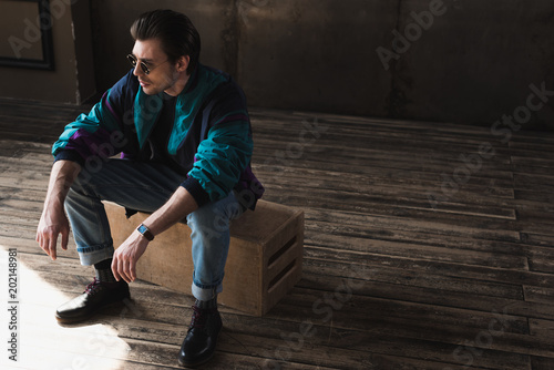 handsome young man in vintage windcheater sitting on wooden box in loft room