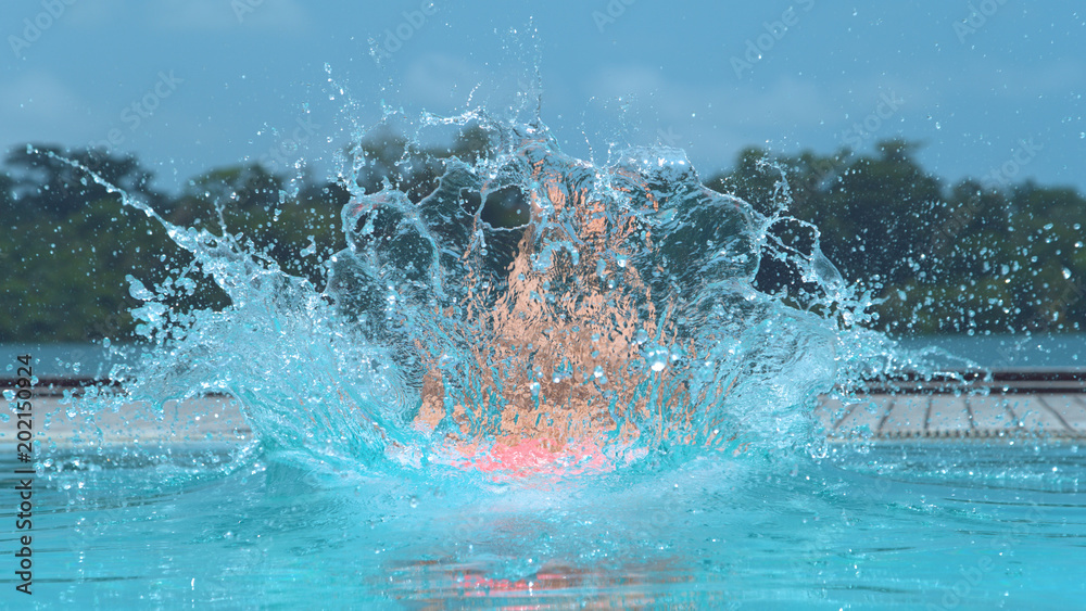 CLOSE UP: Glassy water droplets are sent flying after active woman jumps in pool