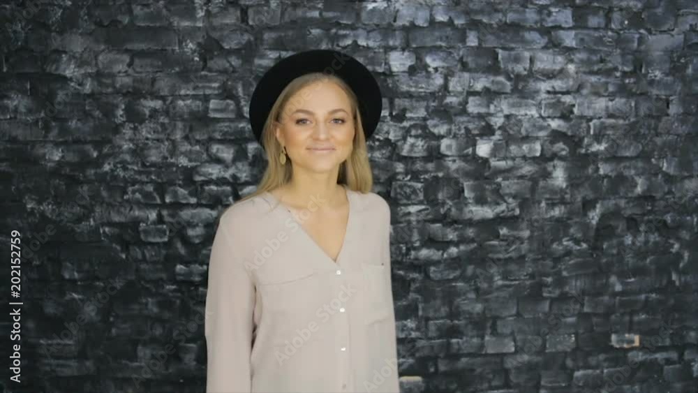 A girl in a black hat is dancing on the background of a textured wall A girl in a black hat is dancing on the background of a textured wall