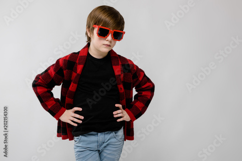 Cute confident little caucasian boy in checkered shirt in red sunglasses fooling on grey background