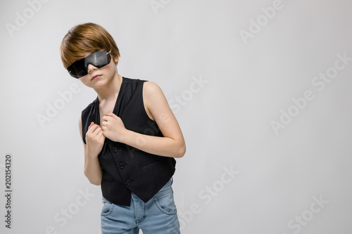 Portrait of adorable surprised little boy standing in studio with sunglasses on grey background