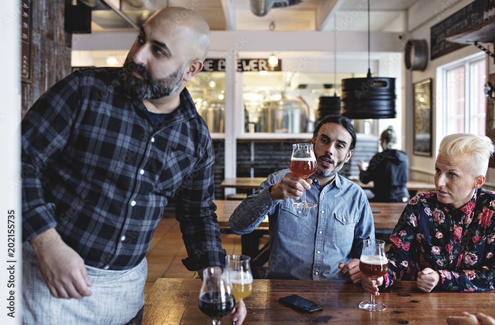 Customers examining various craft beer by bartender at bar Customers examining various craft beer by bartender at bar