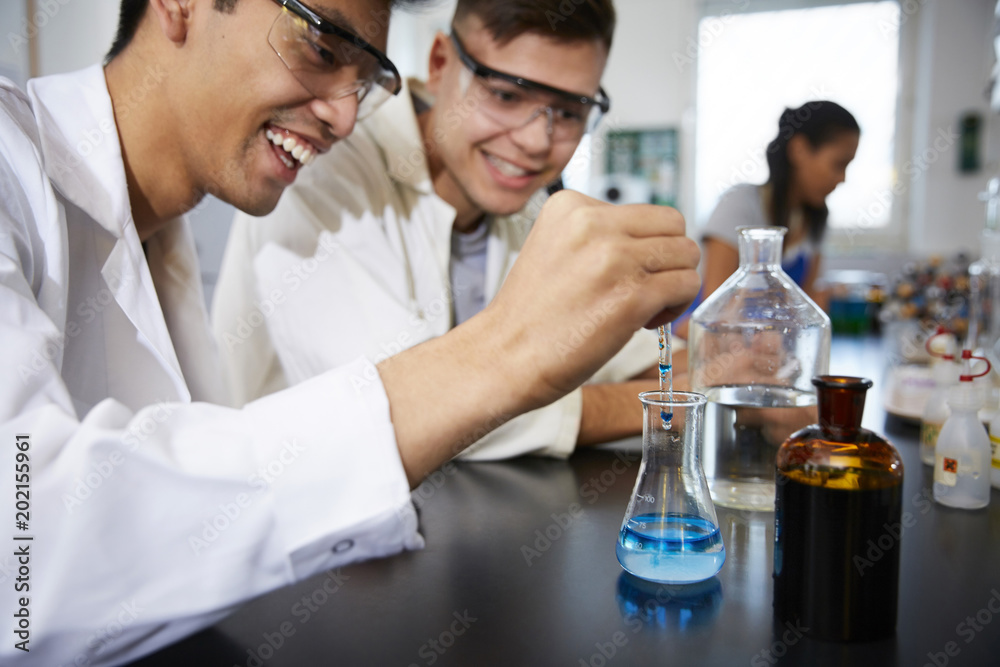 Smiling young male students mixing solutions in glassware at chemistry laboratory Smiling young male students mixing solutions in glassware at chemistry laboratory