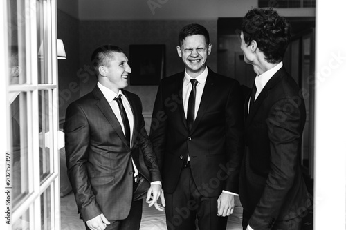 Three men in business suit stand before an open balcony and laugh