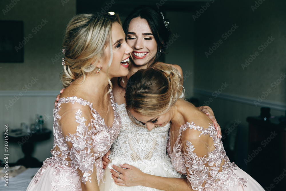 Naklejka premium Bride and bridesmaids laugh posing before an open balcony in a hotel room