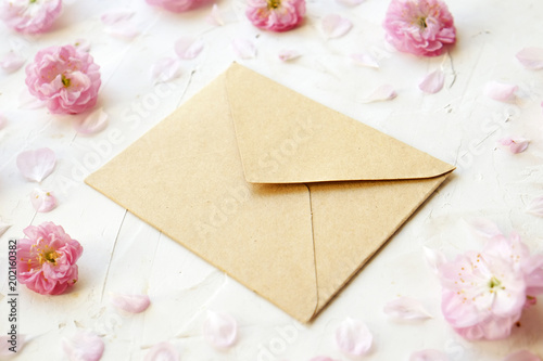 Blank closed craft paper envelope for mother's day with copy space for text among pink flowering blossoms on white background. Minimal composition with flowers and piece of paper. Close up, top view.