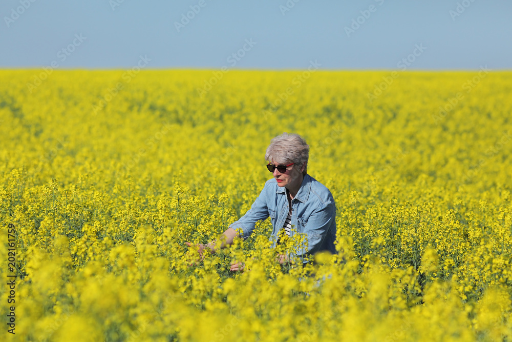 Female agronomist or farmer examining blossoming canola field, rapeseed plant in early spring