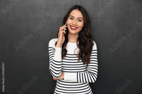 Smiling brunette woman in sweater talking by smartphone