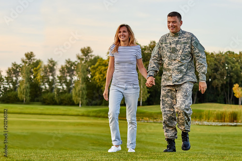 Soldier walking with wife holding hands. Happy man with girlfriend in the park lawn.