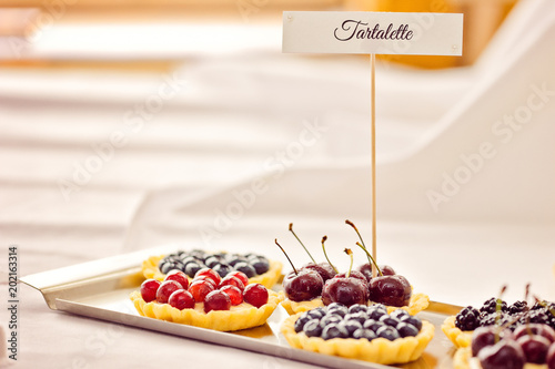 Tasty sweet fruit tartalettes with various fruits and description flag on white background photo