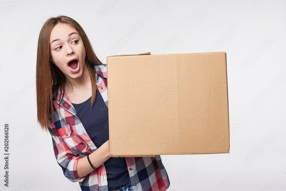 Delivery, relocation and unpacking. Excited young woman holding cardboard box, looking at blank copy space at box, surprised, isolated Delivery, relocation and unpacking. Excited young woman holding cardboard box, looking at blank copy space at box, surprised, isolated