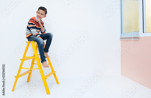 Young boy sat on yellow ladder inside a house
