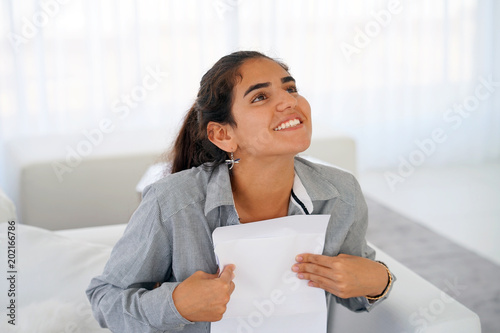 Happy young woman enjoying good news in writing. The girl reads a letter with good news sitting on the couch. An euphoric girl is happy after reading good news in a written letter, approving a loan. photo