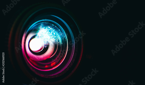 Photo depicts digital projector film presentation. Projector shiny colorful glass lens closeup, macro view, black background.