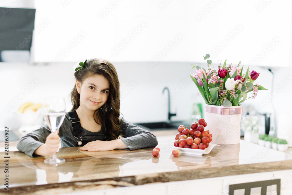 A cute little girl sits in the kitchen, and the plate is placed on the table with grapes.