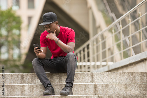 Young man in pink t-shirt looking down to smart phone in city street