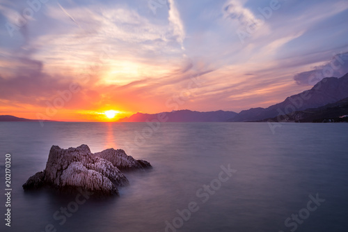 Langzeitbelichtung - Farbenfroher Sonnenuntergang mit Felsen, Gebirge und Wolken am Meer III