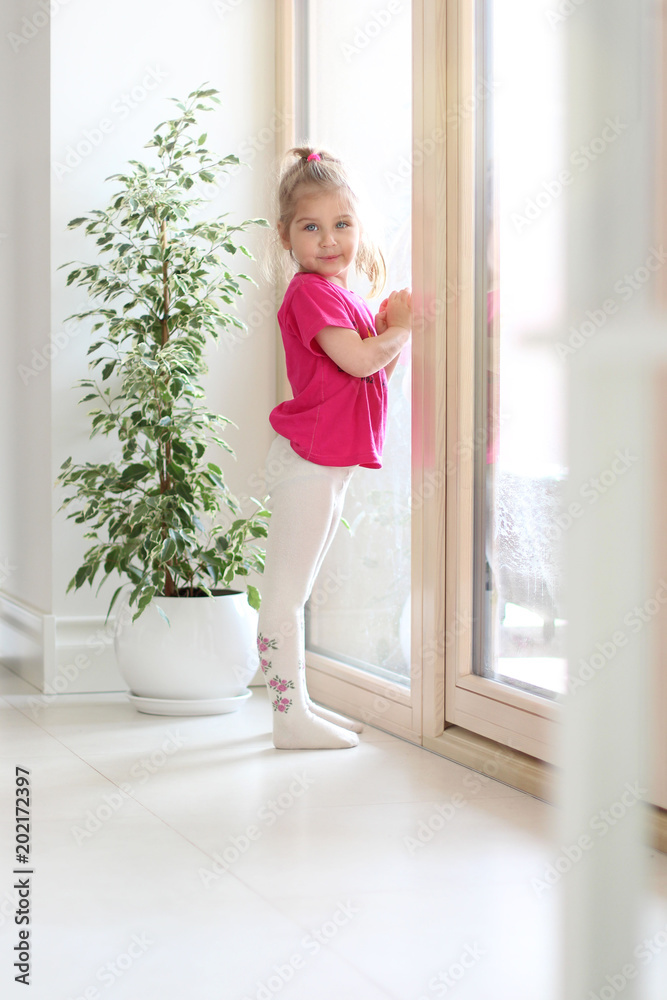 A beautiful cute little girl is standing by the window in the house. Pending. A beautiful cute little girl is standing by the window in the house. Pending.