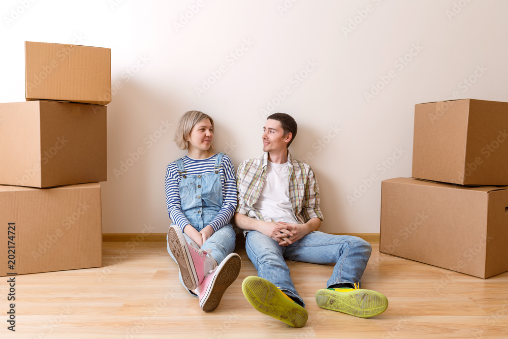 Photo of young married couple sitting on floor among cardboard boxes Photo of young married couple sitting on floor among cardboard boxes