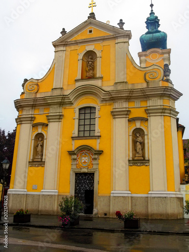 Facade of the Carmelite Church in Gyor (Hungary) from the front in a summer rainy day. Undistinguished yellow Baroque temple with a facade in an Italian style against the gray sky and the wet asphalt