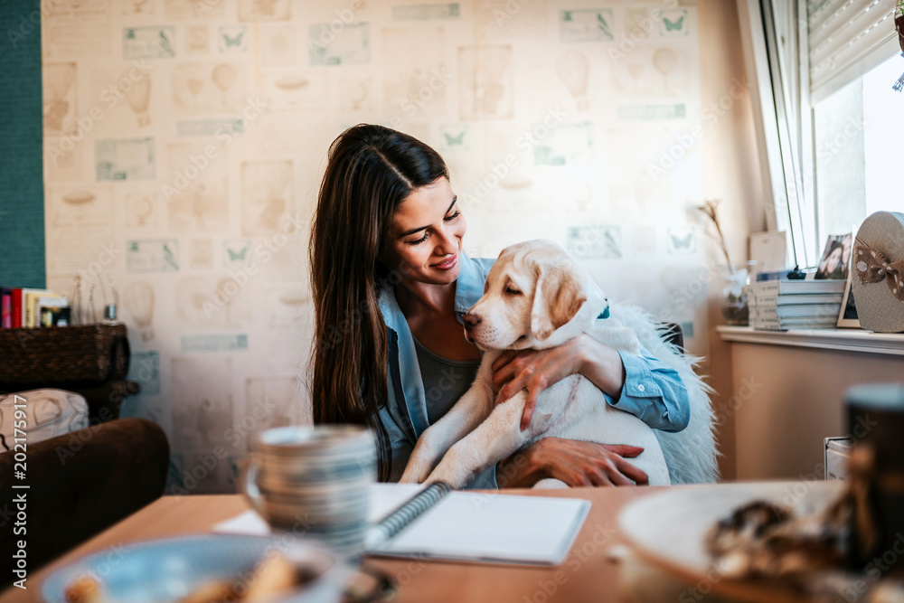 Woman sitting by the table in her apartment with cute puppy. Woman sitting by the table in her apartment with cute puppy.