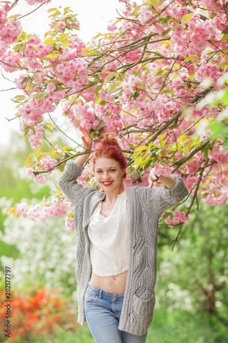 Beautiful young woman with red hair having fun standing in cherry blossom tree, springtime garden mood