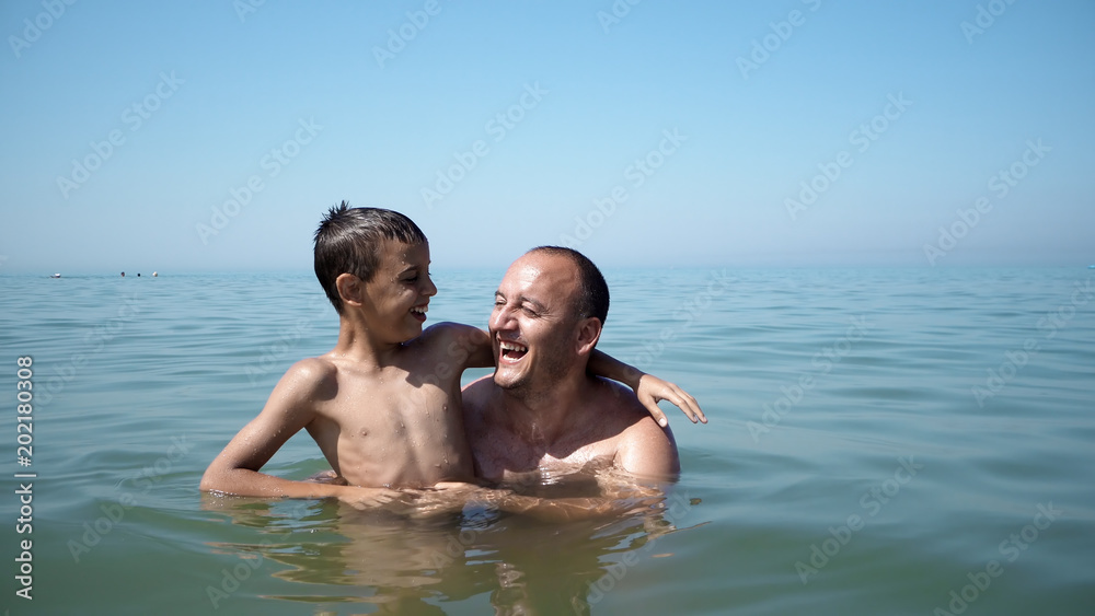 Father and son playing at beach together portrait fun happy lifestyle, boy embrace father and show victory successful gestures Father and son playing at beach together portrait fun happy lifestyle, boy embrace father and show victory successful gestures