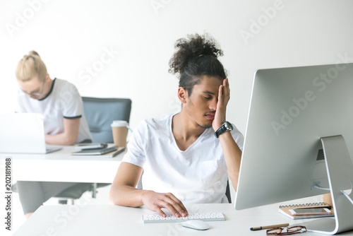 tired young african american man working with desktop computer in office
