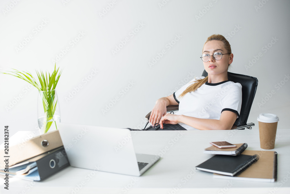beautiful young blonde businesswoman in eyeglasses looking at camera while sitting at workplace beautiful young blonde businesswoman in eyeglasses looking at camera while sitting at workplace