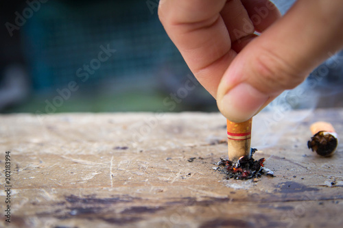 Soft focus of hand putting out a cigarette butt on wooden floor.Stop smoking-World no tobacco day concept.
