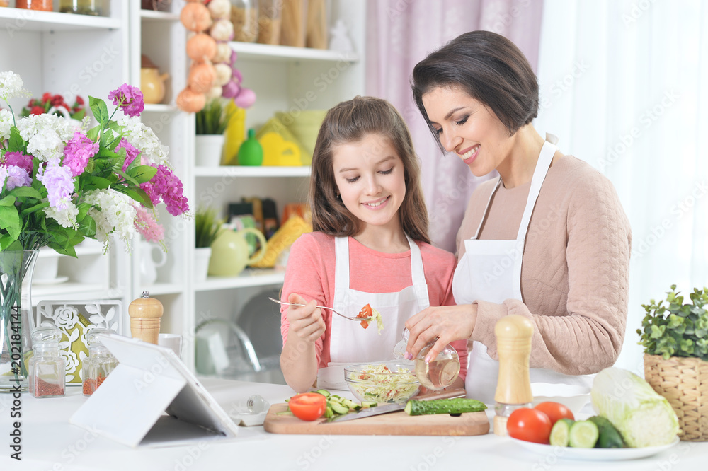 Smiling mother and daughter cooking together at kitchen