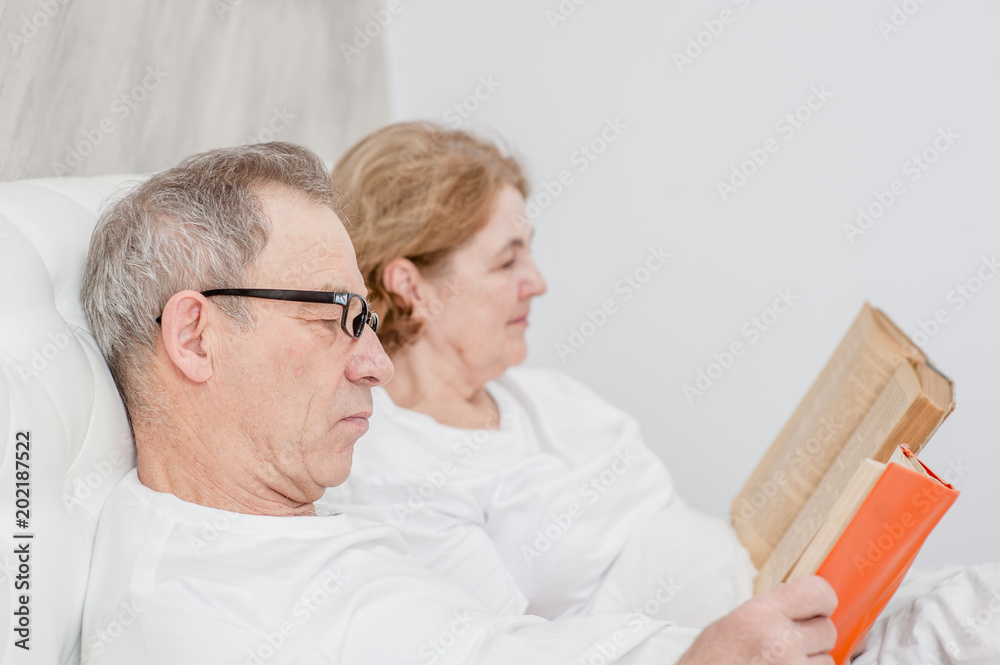 Fototapeta premium elderly couple reading a book on the bed