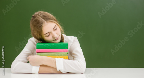 Teen girl sleeping on books in classroom. Space for text