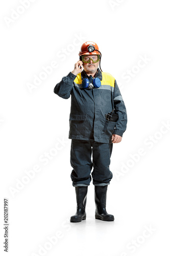 The studio shot of serious senior bearded male miner standing at the camera with smartphone on a white background.