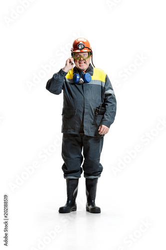 The studio shot of angry senior bearded male miner standing at the camera with smartphone on a white background. © master1305
