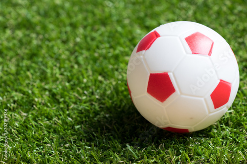 Toy red and white color football on artificial green grass background