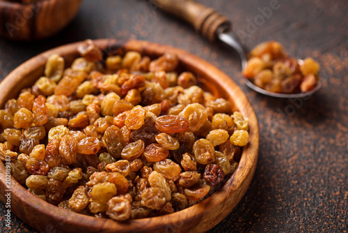 Raisins in wooden bowl on rusty background