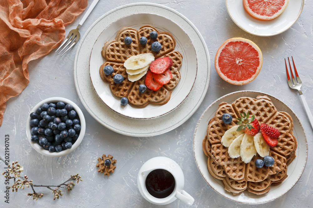 Fototapeta premium Pieces of homemade waffle cake with banana and blueberries on the plates on gray background