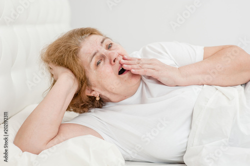 Yawning senior woman on the bed