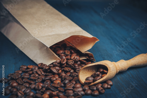 scattered coffee beans from kraft packaging on a blue, wooden background, top view