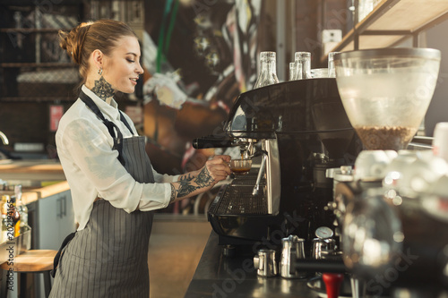 Tattooed barista making coffee in professional coffee machine